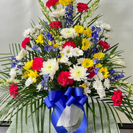 Colorful mixed flower arrangement in a white vase with a blue ribbon