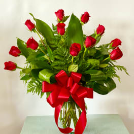 Red roses arranged in a clear glass vase with a large red ribbon