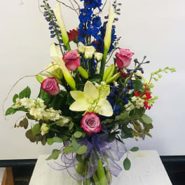 Tall mixed bouquet with blue, pink, white, and red flowers in a glass vase
