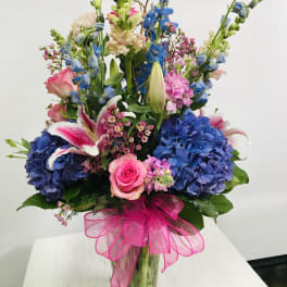 Tall mixed bouquet in a glass vase with blue hydrangeas, pink roses, and lilies