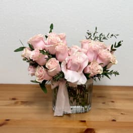 Pink roses arranged in a clear glass vase with a pale ribbon