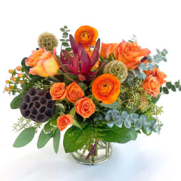 Orange roses and ranunculus in a glass vase with mixed greenery