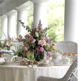 Tall pink and white floral centerpiece on a dining table with teacups