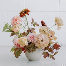 Peach and cream floral arrangement in a white vase with autumn leaves
