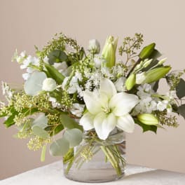 White lilies and mixed white flowers in a clear glass vase