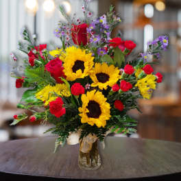 Bouquet of sunflowers, red roses, and purple daisies in a glass vase