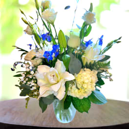White lilies and blue flowers arranged in a glass vase