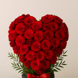 Heart-shaped arrangement of red roses in a black box with a red ribbon