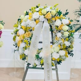 Yellow and white rose wreath on an easel with a memorial ribbon