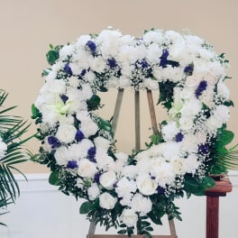 Heart-shaped floral wreath of white roses and purple accents on an easel