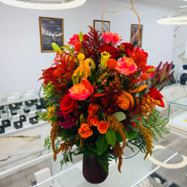 Large mixed bouquet of red, pink, and orange flowers in a dark vase