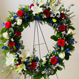 Circular floral wreath with red and white roses, white lilies, and blue accents