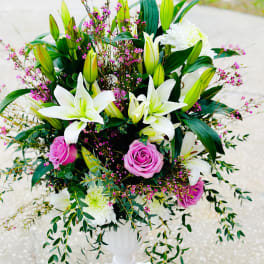 White lilies and pink roses arranged in a white pedestal vase