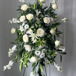 Tall white floral standing spray with roses and daisies on a black easel