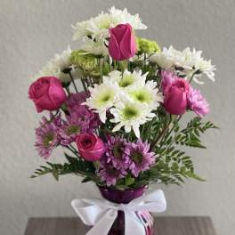 Pink roses and white daisies in a purple vase with a white ribbon