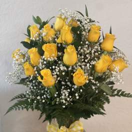 Yellow roses in a clear glass vase with white baby's breath and a gingham ribbon