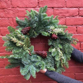 Evergreen wreath with pinecones against a red brick wall