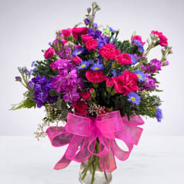 Colorful bouquet of pink, purple, and blue flowers in a glass vase with a pink ribbon