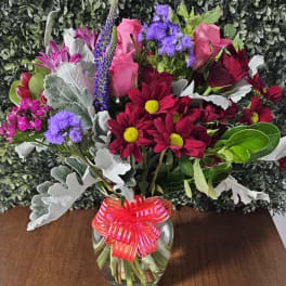Mixed bouquet of pink, red, purple, and white flowers in a glass vase with a ribbon