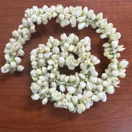Two white flower garlands arranged in loops on a wooden surface