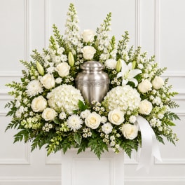 White floral funeral arrangement with a silver urn and ribbon