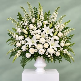 White floral arrangement in a white urn vase with lilies and roses