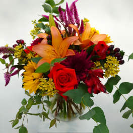Mixed bouquet with orange lilies, red roses, and yellow flowers in a glass vase