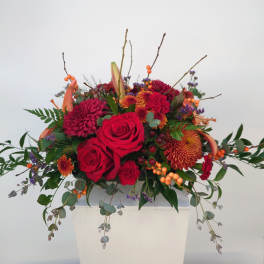 Red roses and orange mums in a white vase with trailing greenery