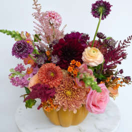 Mixed bouquet in a pumpkin-shaped vase with pink, purple, peach, and orange blooms.