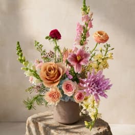 Mixed bouquet in a taupe vase with pink, peach, purple, and white flowers