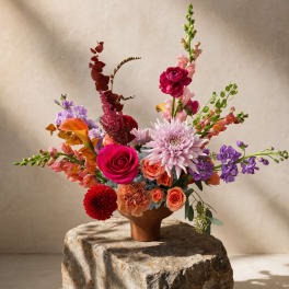 Colorful mixed flower arrangement in a brown vase on a stone pedestal