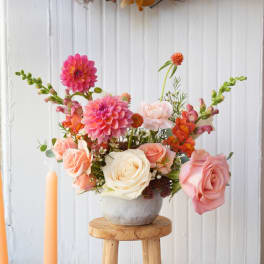 Pink and peach flowers arranged in a white vase on a stool
