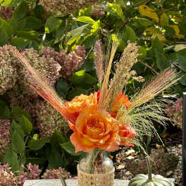 Orange rose arrangement in a glass bottle with pumpkins on a stone ledge