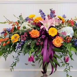 Large colorful floral spray with lilies, roses, and a purple ribbon