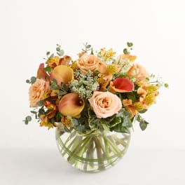 Peach roses and calla lilies in a clear round vase