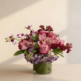 Low arrangement of pink roses and orchids with purple hydrangea in a leaf-lined glass vase