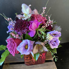 Mixed bouquet of pink, purple, and lavender flowers in a red glass vase