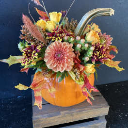 Fall floral arrangement in a pumpkin container with yellow and peach blooms