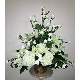 White floral arrangement in a woven basket with lilies and carnations
