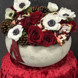 Red roses and white anemones in a round vase with pinecones and pomegranate pieces