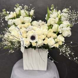 White floral arrangement in a tall square vase with roses and tulips