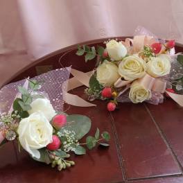 Two small rose bouquets with pink ribbon and greenery on a wooden bench