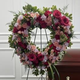 Heart-shaped floral wreath on a stand with pink and purple flowers