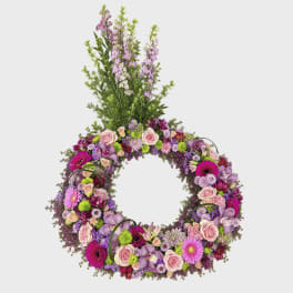 Circular floral wreath with pink and purple flowers and a tall top spray