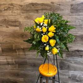 Yellow rose arrangement on a tall stand with greenery and white filler flowers