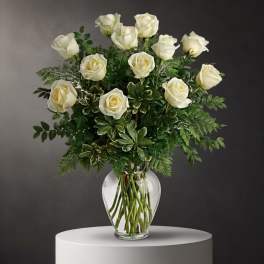 White roses arranged in a clear glass vase with mixed greenery