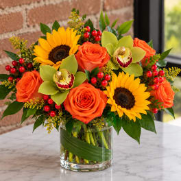Orange roses and sunflowers in a glass vase with green orchids