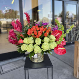 Bright mixed bouquet with roses, anthuriums, and tropical blooms in a gold vase
