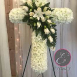 White floral cross on a stand with lilies and clustered white blooms