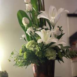 White lilies and roses in a dark vase with green foliage
